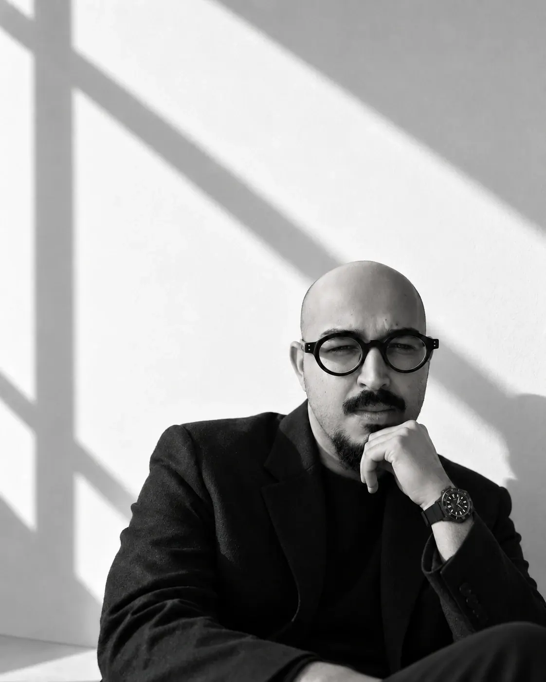 Portrait of Ar. Aniruddh Dubey, partner at S+UM Architects, wearing a black wristwatch and seated against a wall with architectural shadows