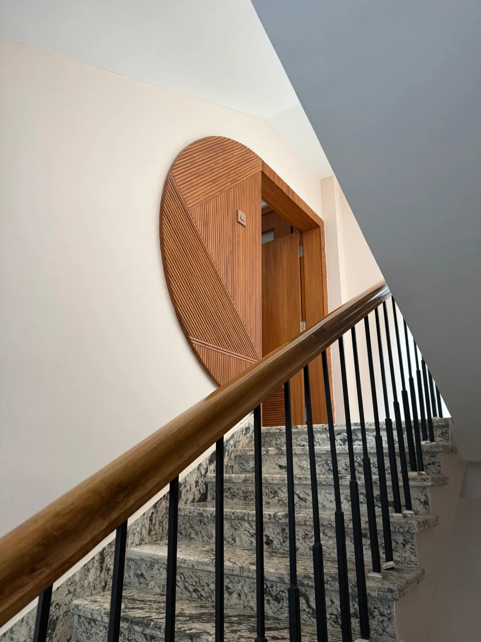 Interior staircase with a warm timber handrail, dark balusters and a rounded timber door surround